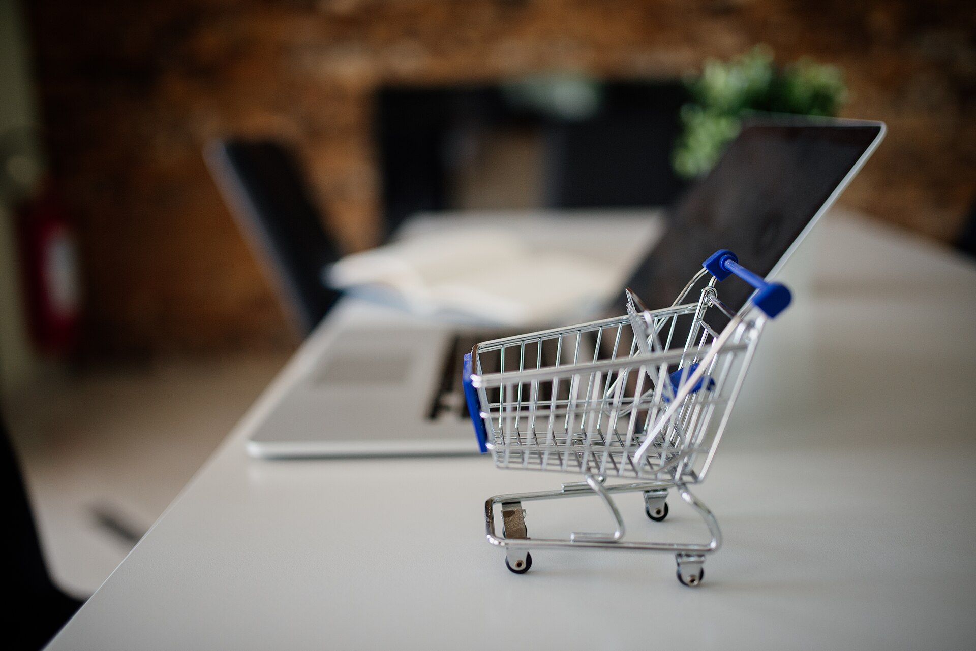 Carrinho de compras em miniatura ao lado de um notebook sobre uma mesa