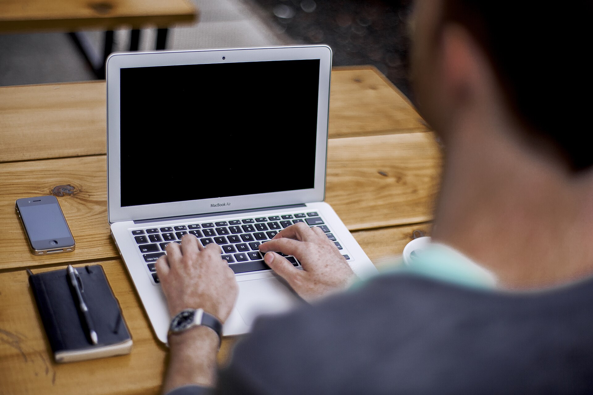 Pessoa digitando em um notebook sobre uma mesa de madeira